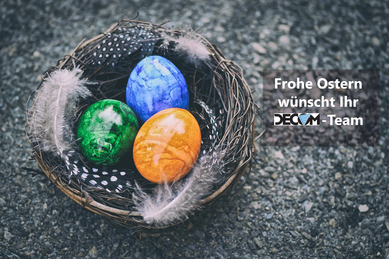 Grauer Hintergrund. Aus Ästen feflochtenes Nest, mit kleinen Federn verziert. Drei bemalte Ostereier (blau, gelb, grün). In weißem Schriftzug steht "Frohe Ostern wünscht Ihr DECOM Team".